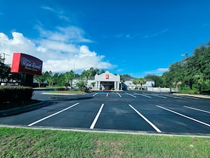 A Red Roof Inn & Suites with a clear blue sky, parking lot, and surrounding greenery. - Red Roof Inn & Suites Hinesville (Hinesville)