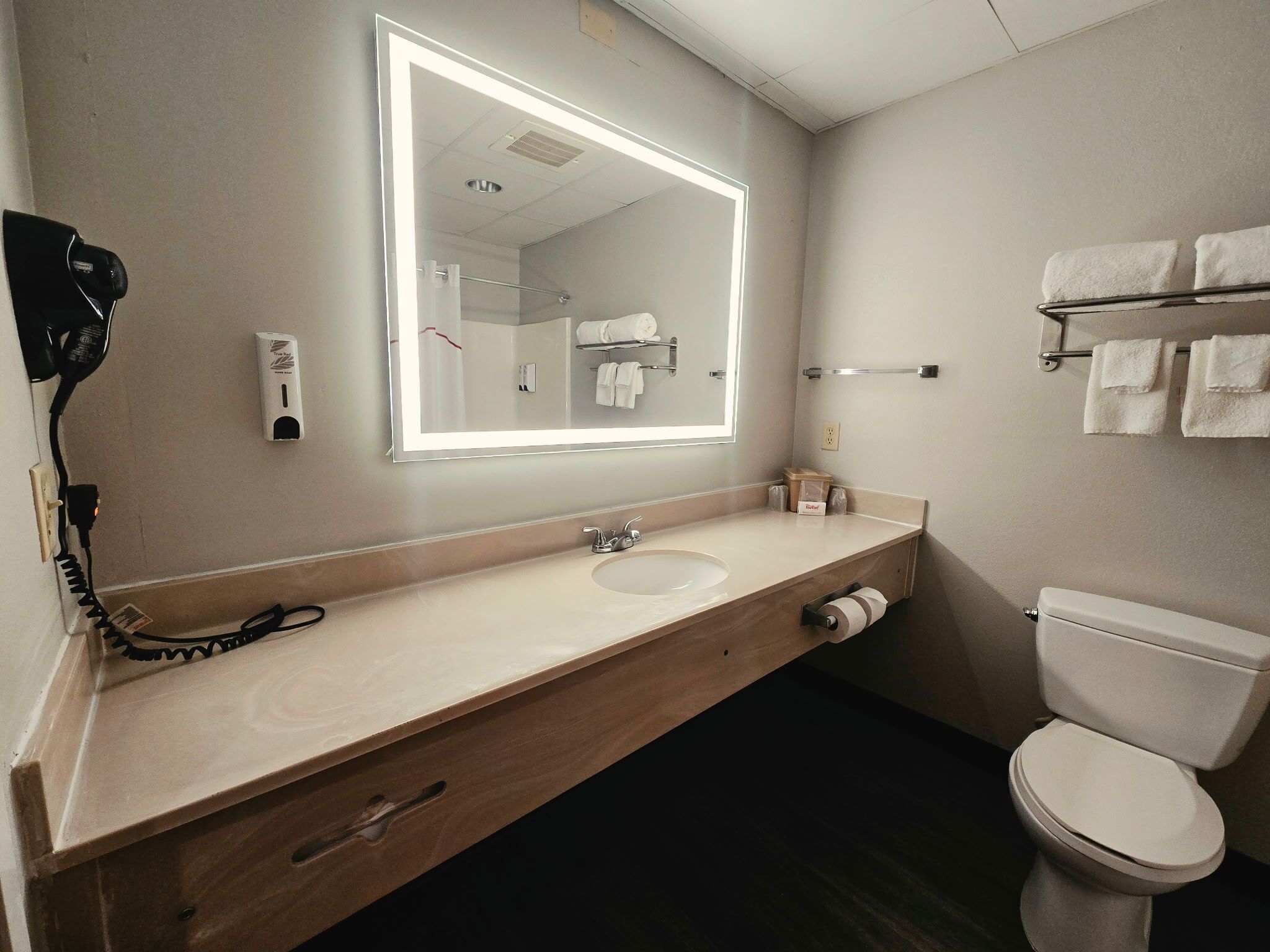 A hotel bathroom with a large mirror, a sink, a toilet, and a towel rack.