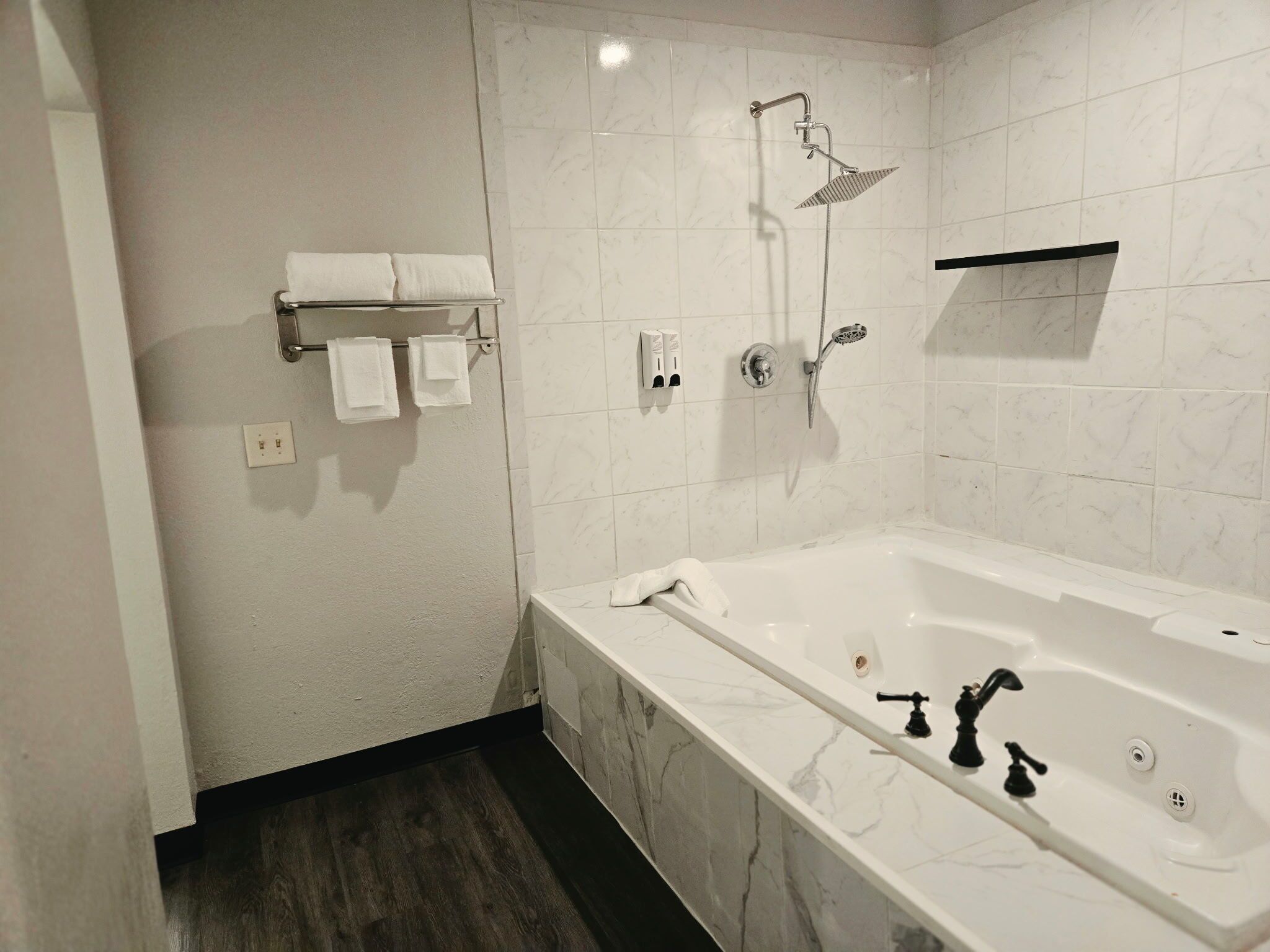 A modern bathroom with a marble bathtub, a shower with a handheld showerhead, and a towel rack with neatly folded towels.
