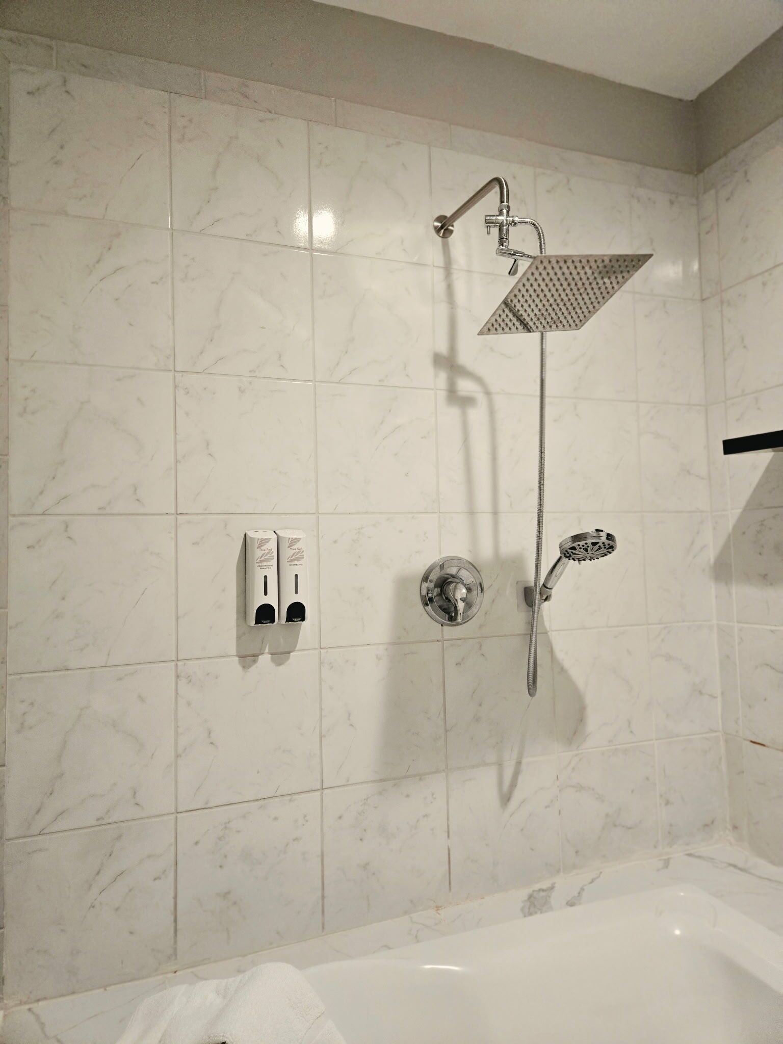 A bathroom with a shower, a bathtub, and two soap dispensers on the wall.