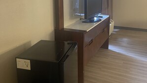 Une pièce avec une commode en bois, un téléviseur posé dessus et un petit appareil noir sur le sol.