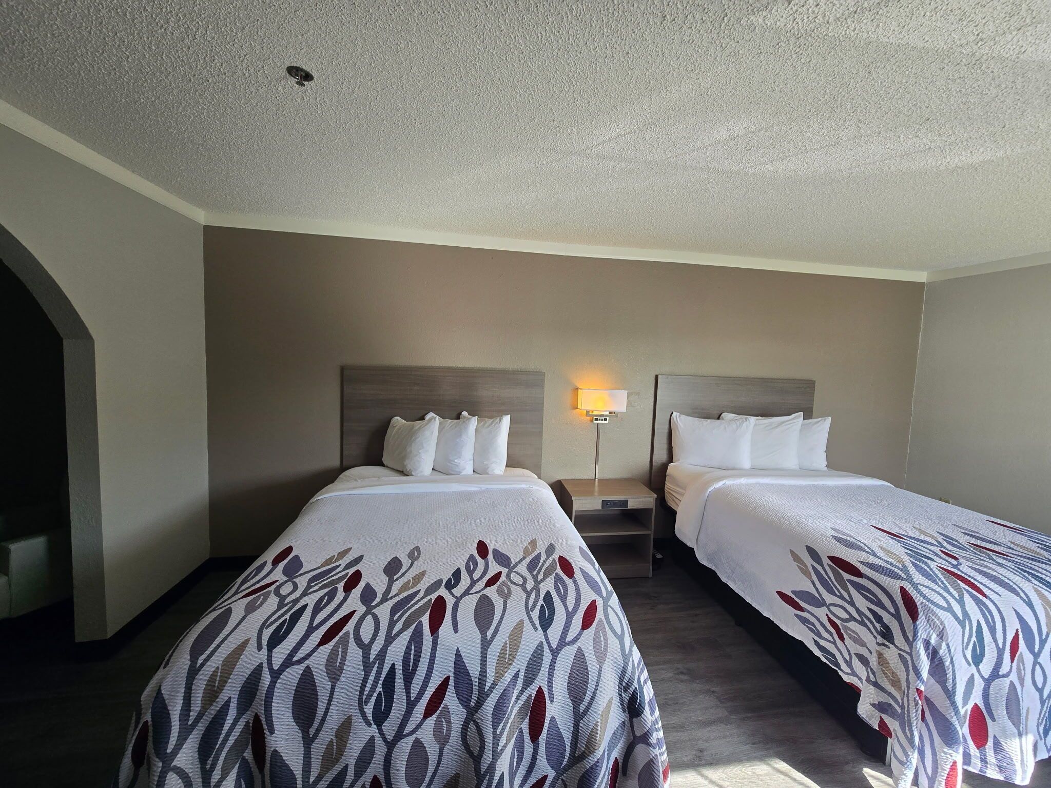 Una habitación de hotel con dos camas, cada una con una colcha estampada, una mesita de noche, una lámpara de pared y una luz de techo.