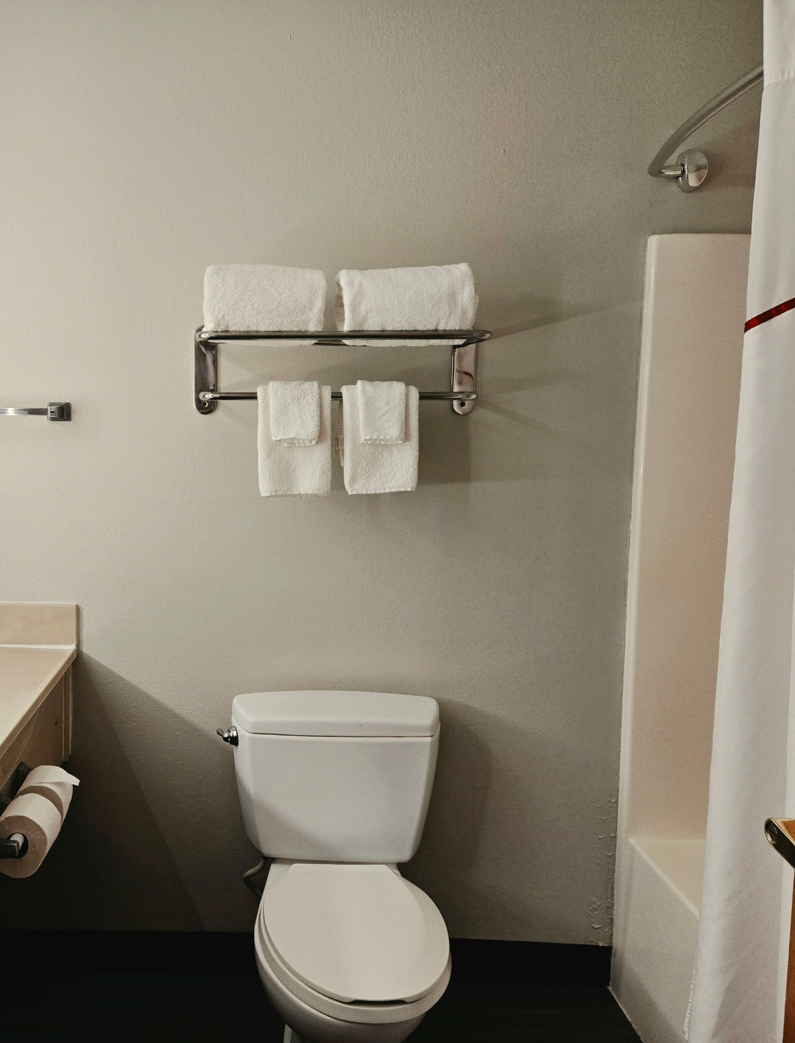 A bathroom with a toilet, a towel rack with towels, a shower curtain, and a toilet paper holder.