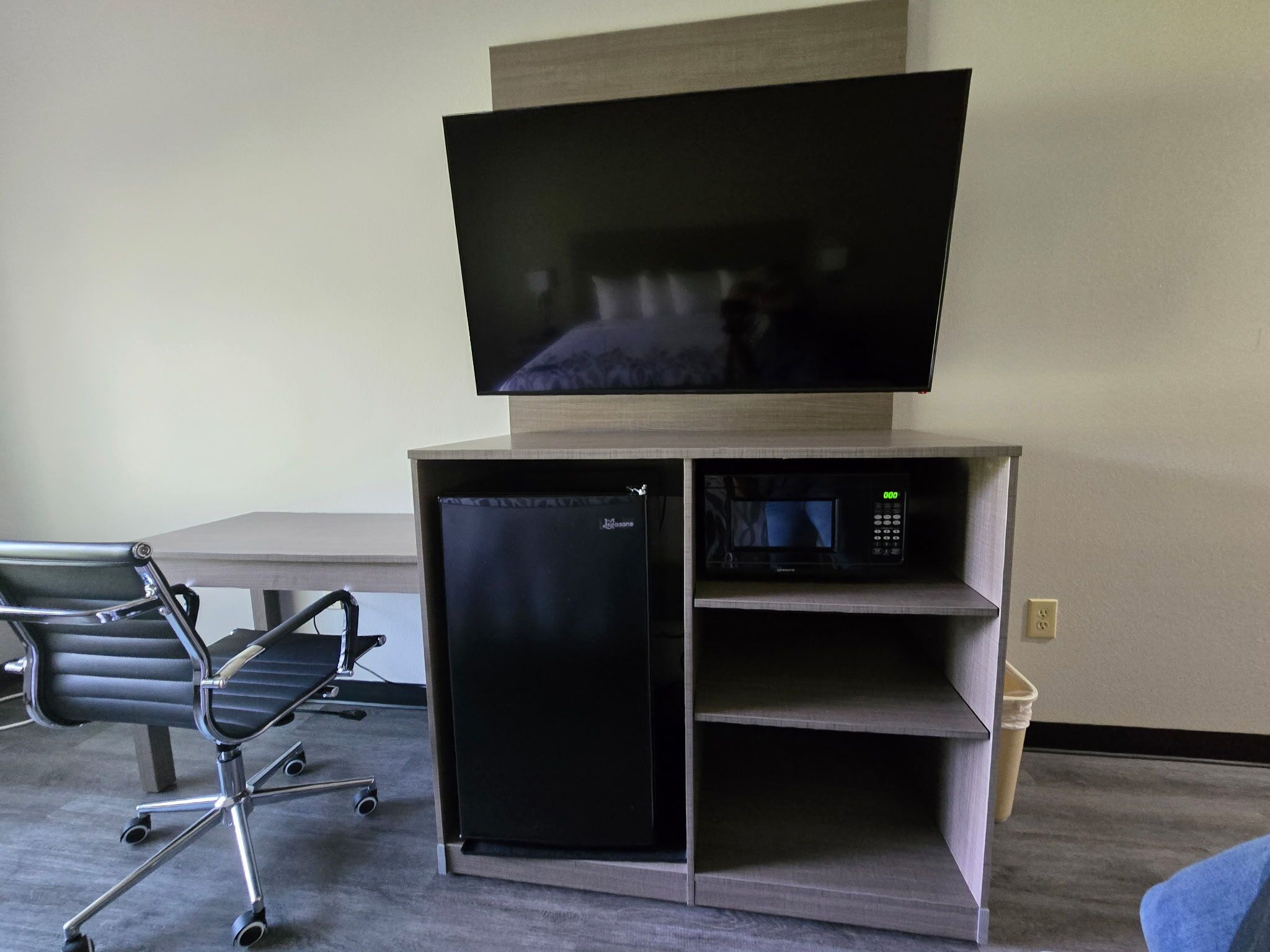 Uma cozinha compacta equipada com geladeira, micro-ondas e uma TV de tela plana em um suporte.