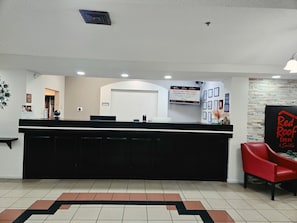 Ein Hotel-Empfangsbereich mit einer schwarzen Theke, einem roten Sessel und einem Schild für Red Roof Inn Suites.