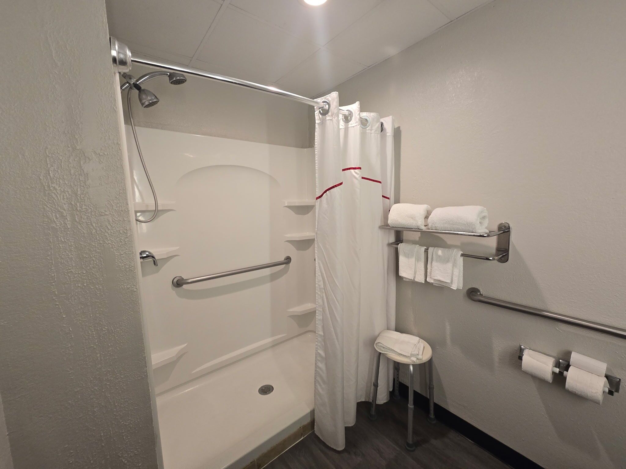 A bathroom with a shower, grab bars, a toilet, and a towel rack.
