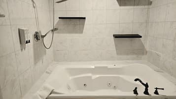 A bathroom with a large bathtub, a handheld showerhead, and two wall-mounted towel racks.