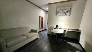 A room with a sofa, a dining table with chairs, a coffee machine, and a lamp.