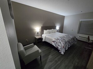 Habitació d'hotel amb llit, tauletes de nit, una cadira i un radiador.