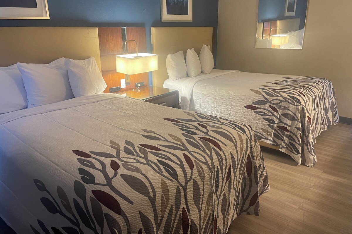 Una habitación de hotel con dos camas, una mesita de noche con lámpara y obras de arte en las paredes.