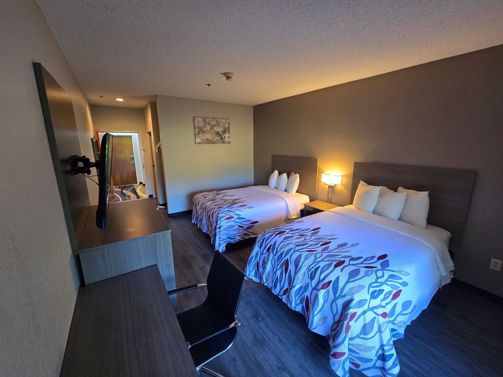 A hotel room with two beds, a desk, and a mirror.