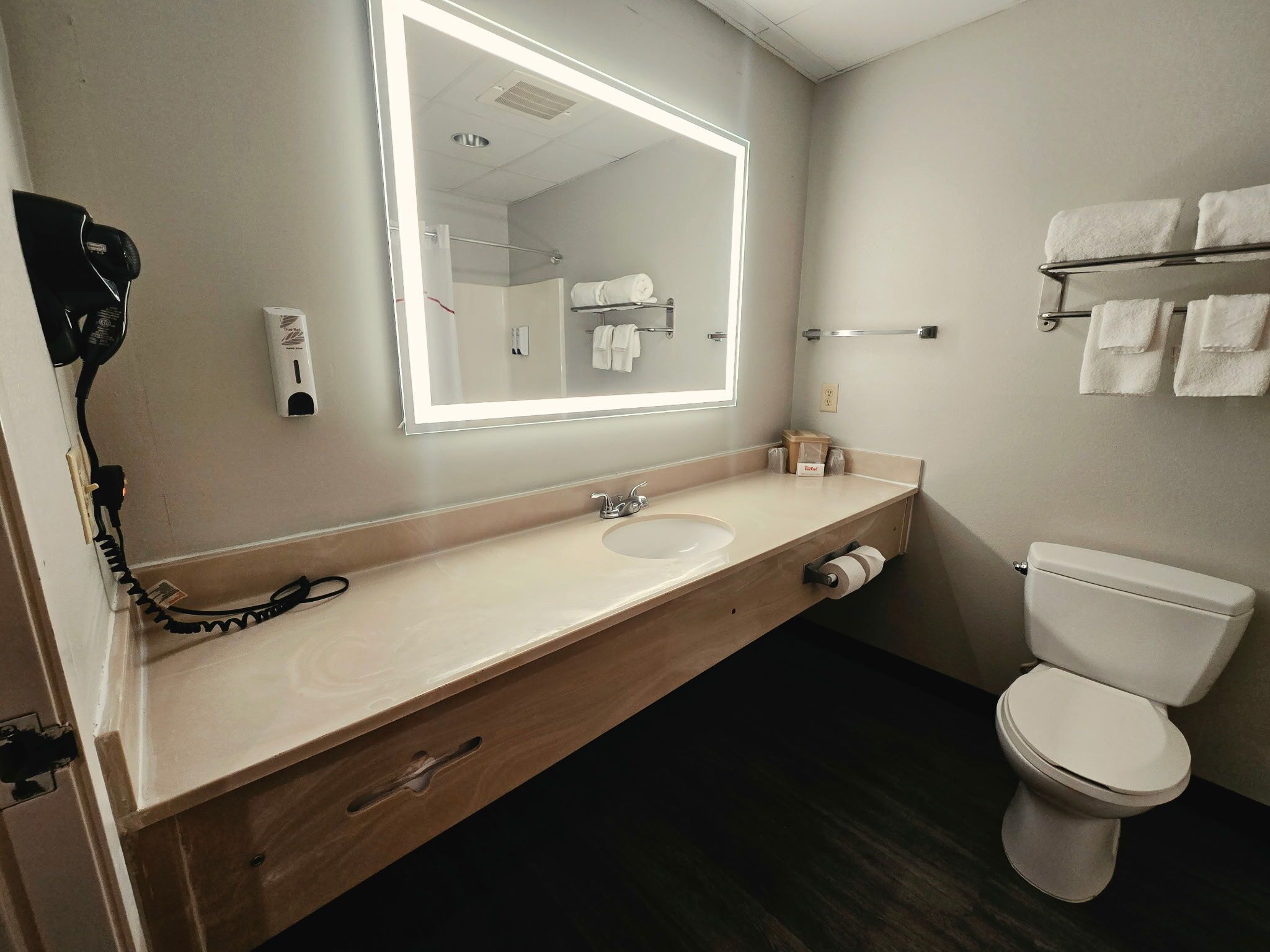 A hotel bathroom with a large mirror, a sink, a toilet, and a towel rack.