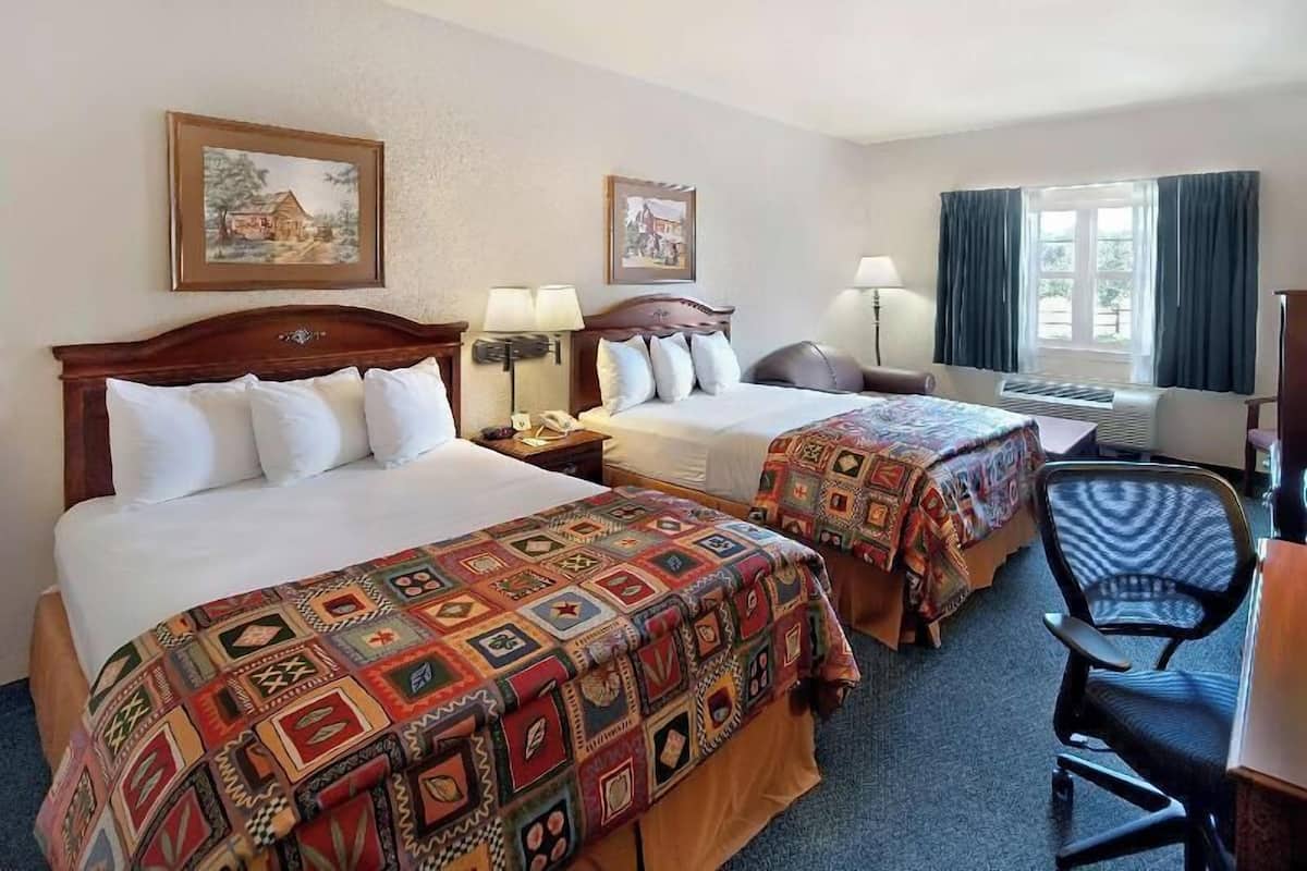 A hotel room with two beds, a desk, a chair, and a window with curtains.