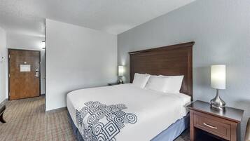 A hotel room with a large bed, a wooden headboard, two bedside tables with lamps, and a door with a sign.