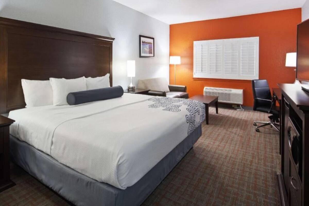 A hotel room with a large bed, a desk with a chair, a TV, and a window with blinds.
