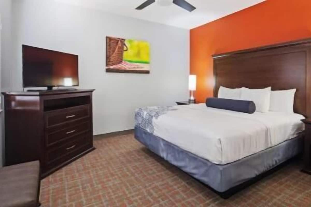 A hotel room with a bed, a dresser, a television, and a painting on the wall.