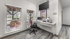 A modern office space with a desk, computer, and chair, large windows, and a mounted TV. - Best Western Plus Fredericksburg (Fredericksburg)