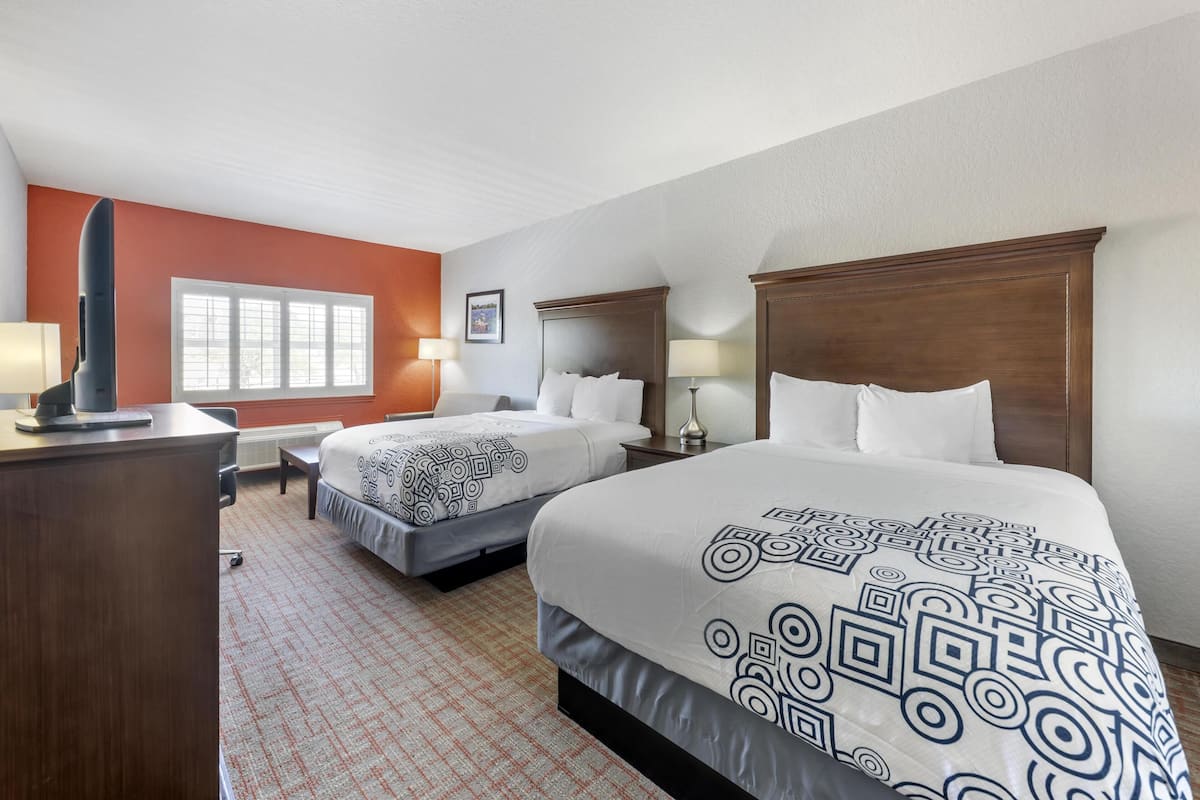 A hotel room with two beds, a desk, and a window.