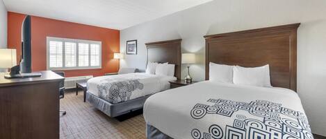 Quarto de hotel com duas camas, uma escrivaninha e uma janela.