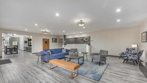 Een moderne woonkamer met een blauwe bank, een houten bankje en een salontafel. Op de achtergrond is een eetgedeelte met een tafel en stoelen.