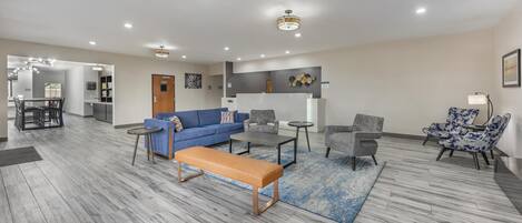 A modern living room with a blue sofa, a wooden bench, and a coffee table. There is a dining area in the background with a table and chairs.