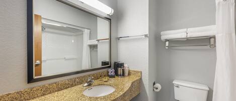 Un baño con lavamanos de encimera de granito, un espejo, inodoro y toallero.