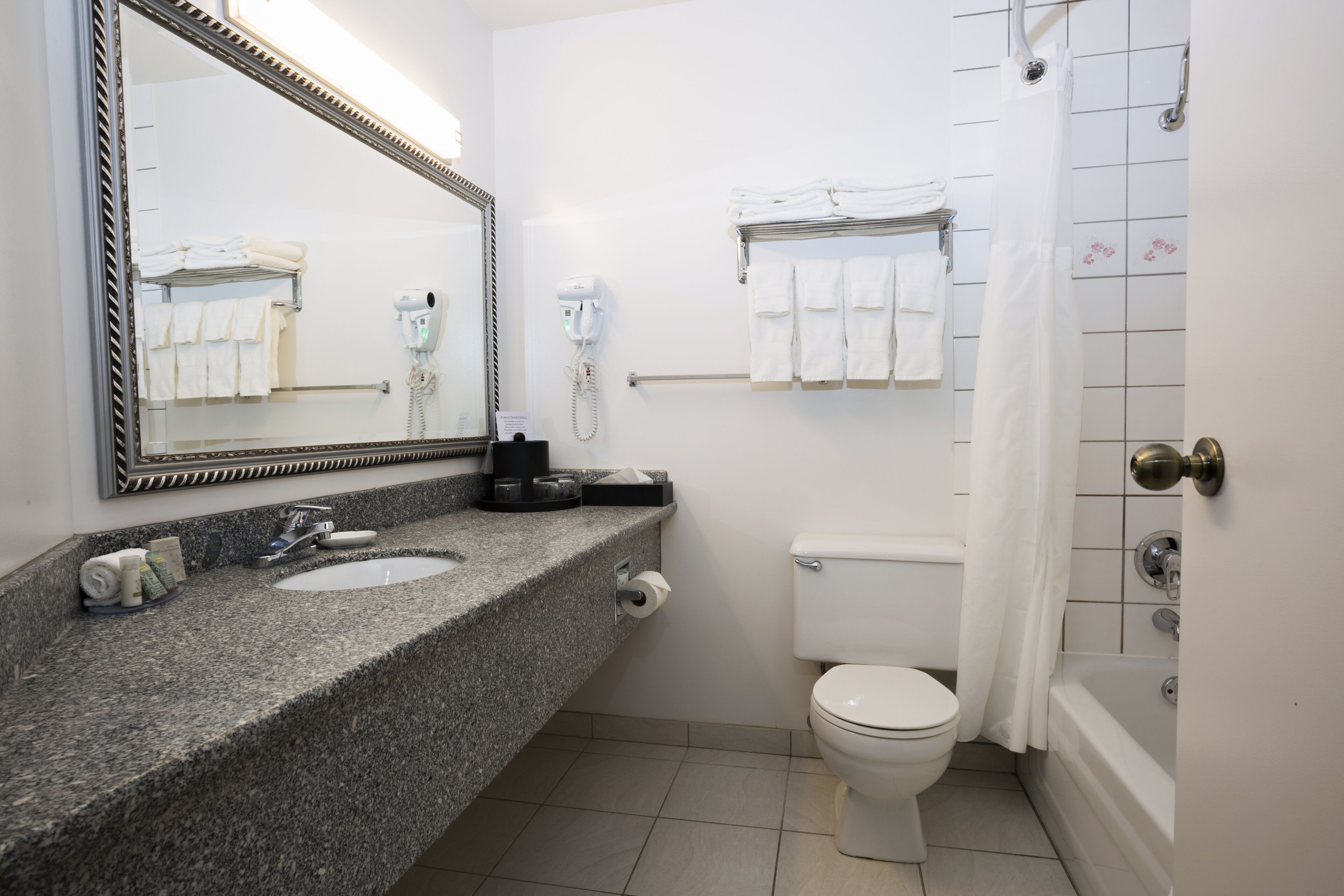 Un baño con lavamanos de encimera de granito, un espejo, un inodoro, una ducha con cortina y un perchero con toallas dobladas.