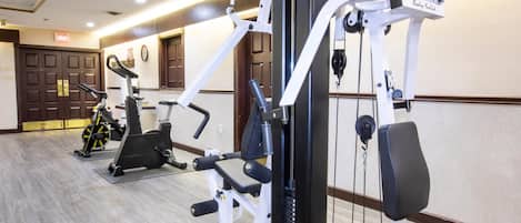 A gym with various exercise machines, a bench, and a wall-mounted clock.