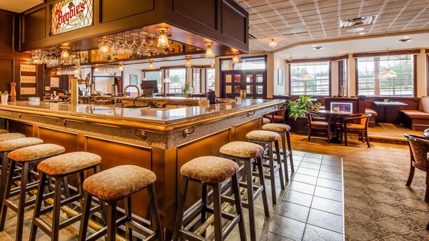 A bar area with a central island, multiple stools, and a seating area with tables and chairs. - Tower Inn and Suites (Quesnel)
