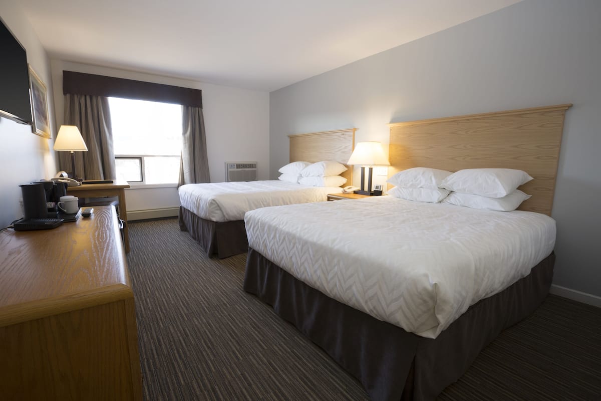 Una habitación de hotel con dos camas, un escritorio con lámpara, un teléfono y una ventana con cortinas.