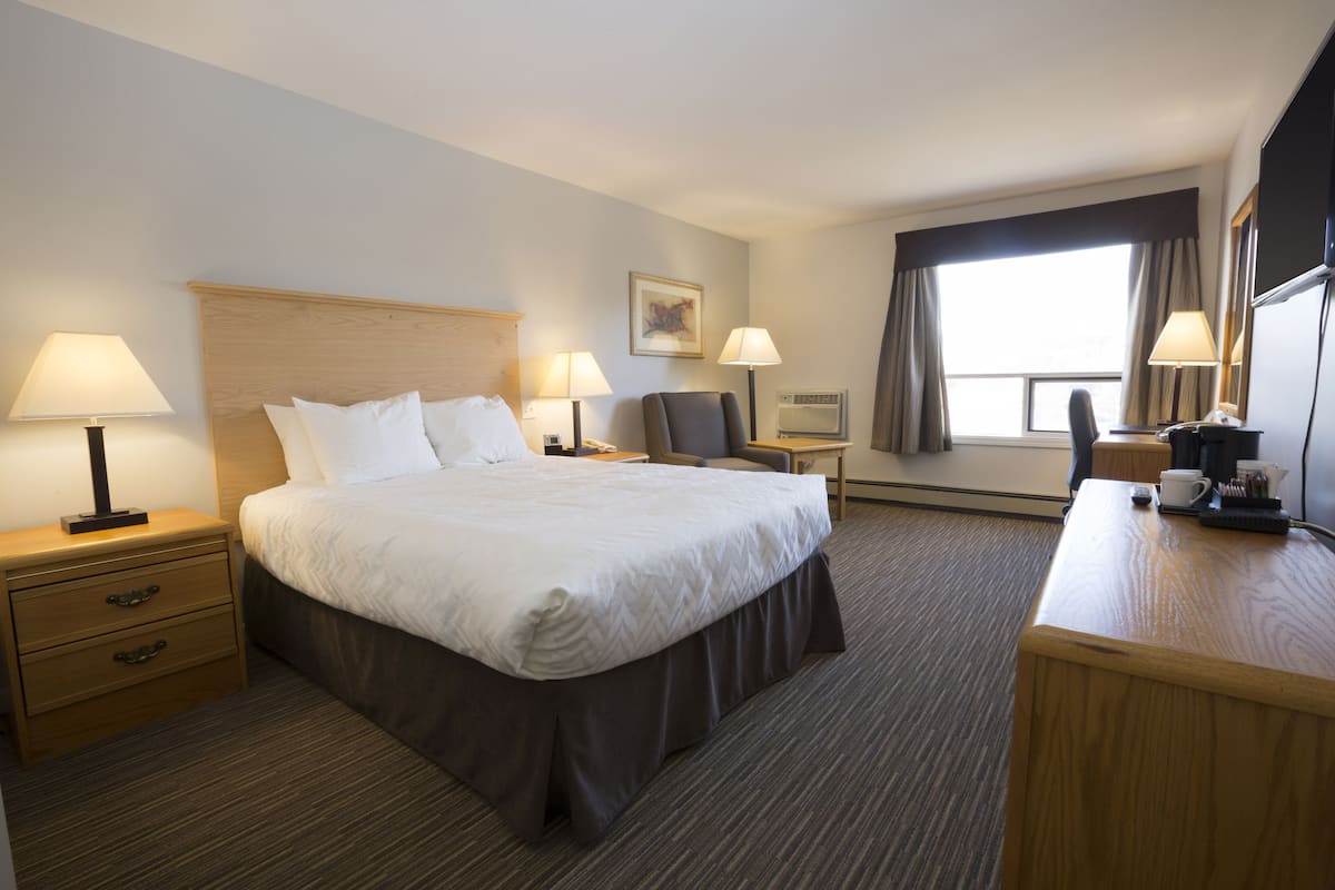 Habitación de hotel con una cama grande, dos mesitas de noche con lámparas, un escritorio con silla, una ventana con cortinas y un televisor de pantalla plana.