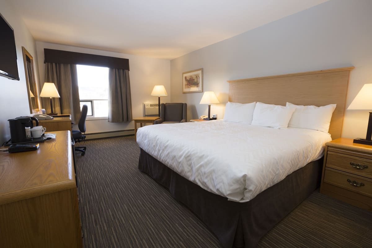 Habitación de hotel con una cama grande, un escritorio con cafetera, dos lámparas, un televisor y una ventana con cortinas.