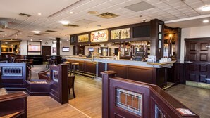 A bar area with a counter, stools, and a large screen. - Tower Inn and Suites (Quesnel)