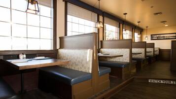A restaurant with booths and tables, featuring a wooden floor and large windows.