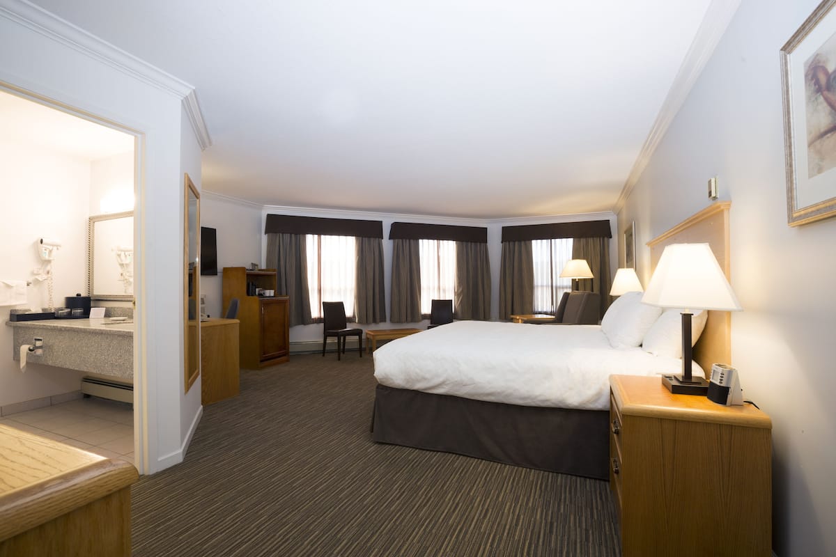 Habitación de hotel con cama, mesita de noche, lámpara, escritorio, silla y baño con espejo y lavabo.