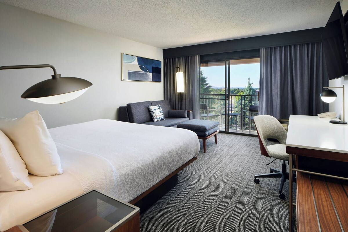 Quarto de hotel com cama grande, escrivaninha, cadeira, sofá e varanda com vista.