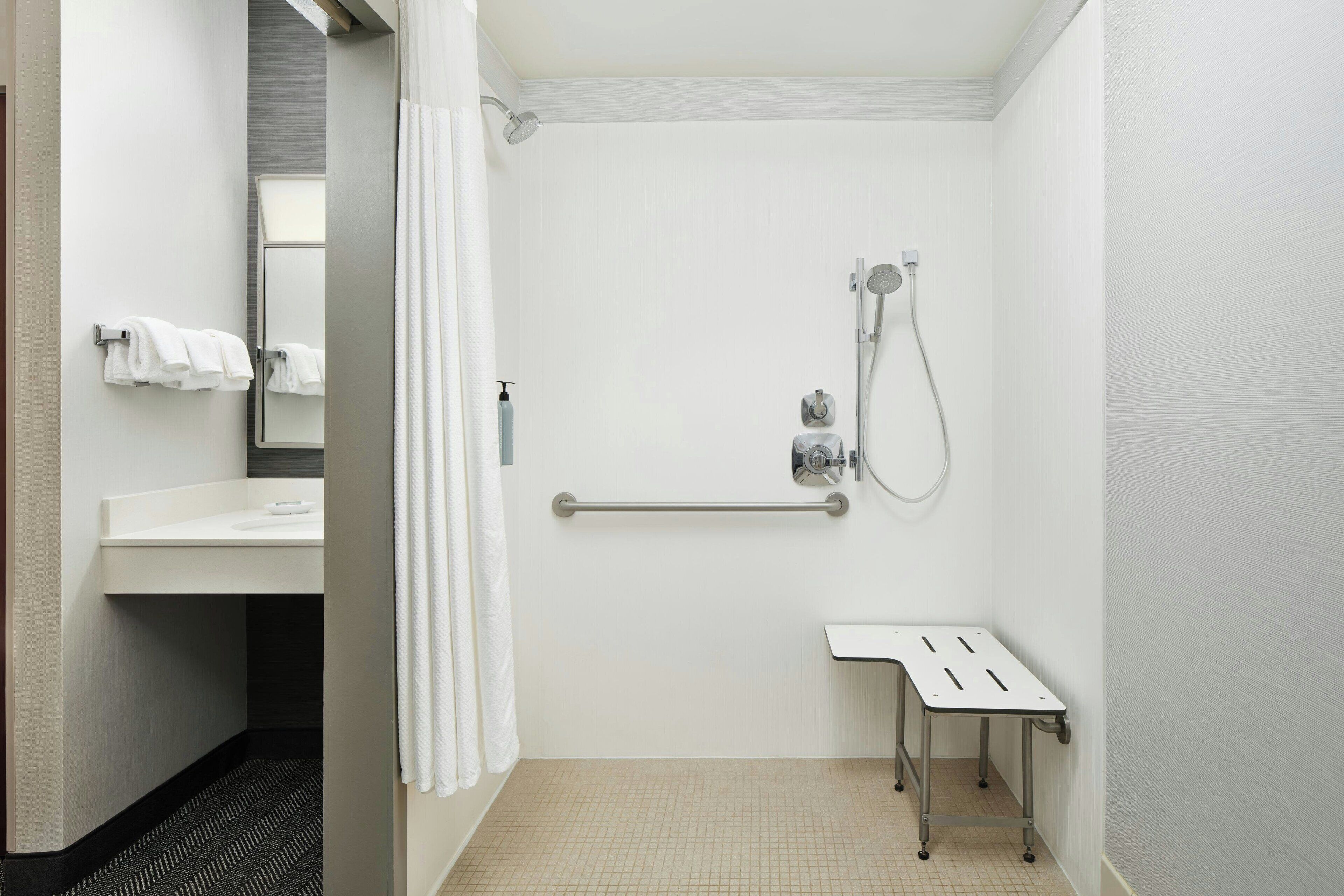 A small, clean bathroom with a shower, a sink, and a grab bar.