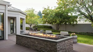A stone fire pit with a fire, surrounded by outdoor furniture, in a landscaped backyard with a house in the background. - Courtyard by Marriott Boulder Longmont (Longmont)