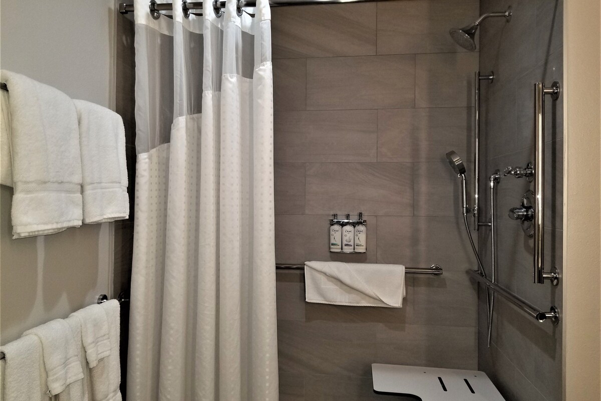 Un espace douche moderne doté d’une porte en verre, d’un porte-serviettes avec plusieurs serviettes et d’un pommeau de douche à main.