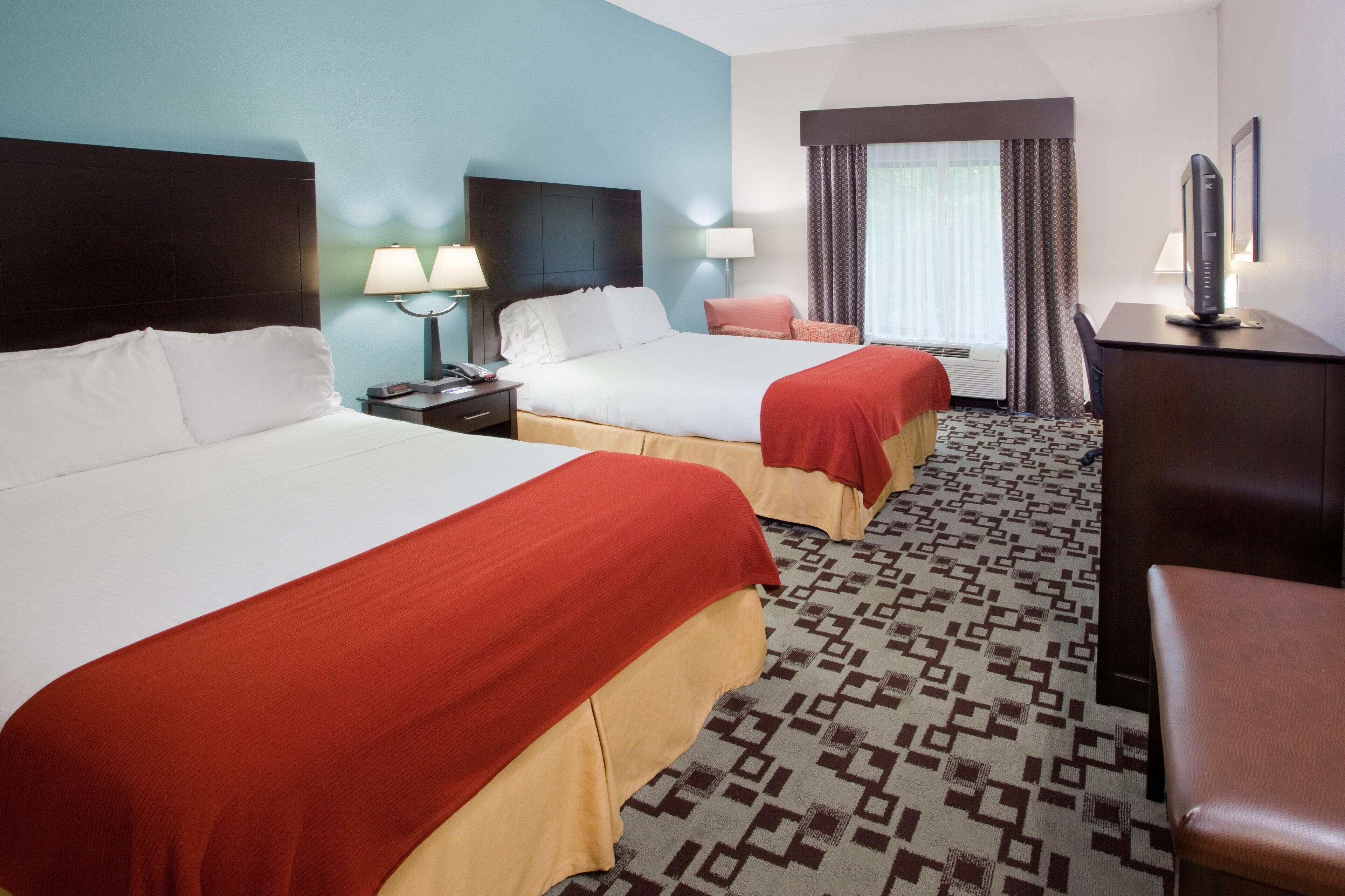 A hotel room with two beds, a desk, a chair, and a television.