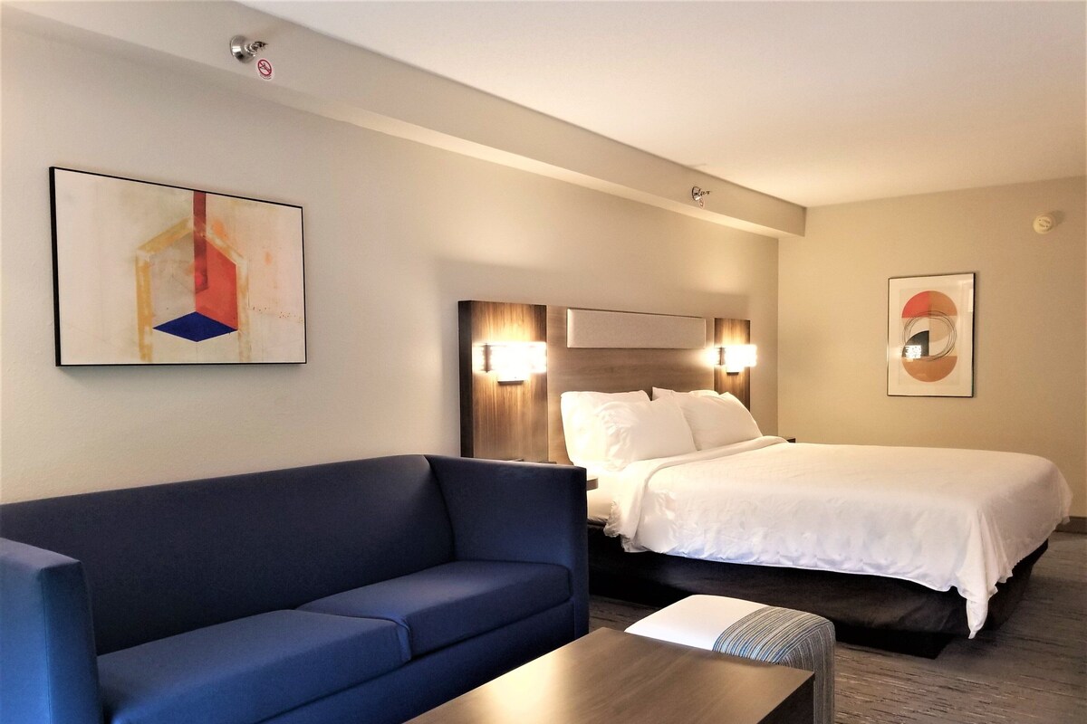 Une chambre d’hôtel avec un lit, un canapé bleu, une table en bois et deux lampes fixées au mur.