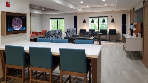 Un espace repas moderne avec une longue table, des chaises bleues et un téléviseur à écran plat fixé au mur.