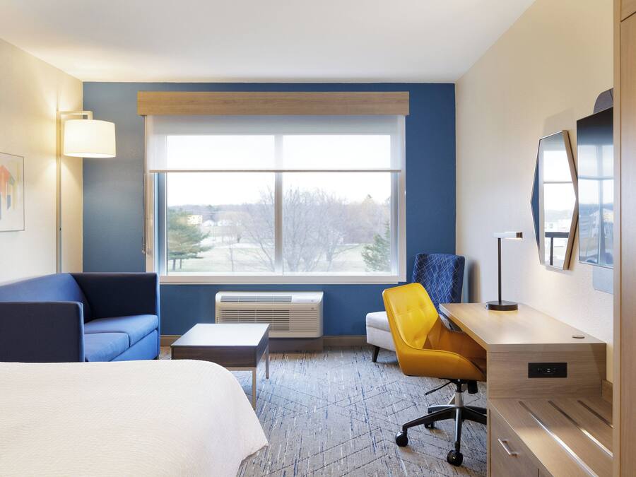 A hotel room with a bed, a desk, a chair, a window with a view, and a wall-mounted TV.