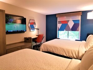 A hotel room with a bed, a desk, a chair, a TV, and a window with a geometric curtain.