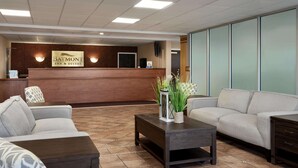 De receptiebalie van een Baymont Inn & Suites, met een houten balie, twee banken, een salontafel en een groot raam met zonwering.