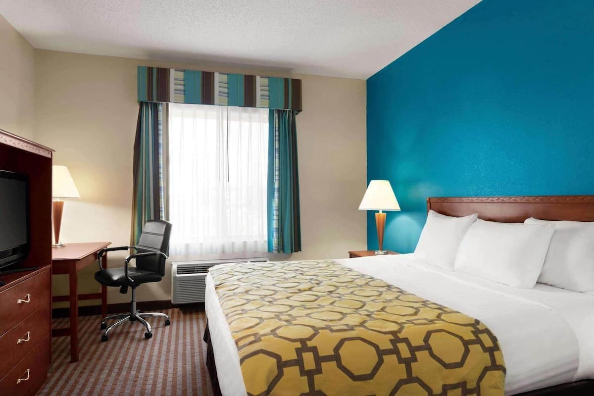 A hotel room with a bed, a desk with a chair, a television, and a window with curtains.