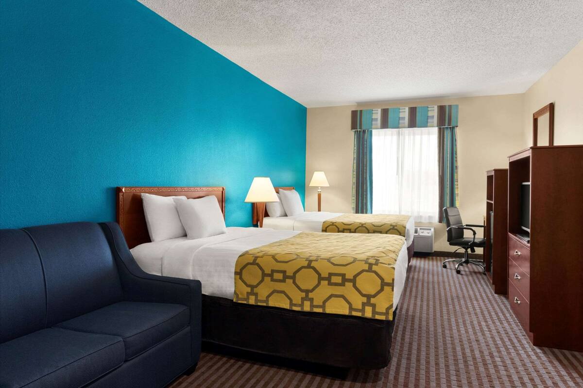 A hotel room with two beds, a sofa, a desk, and a TV.