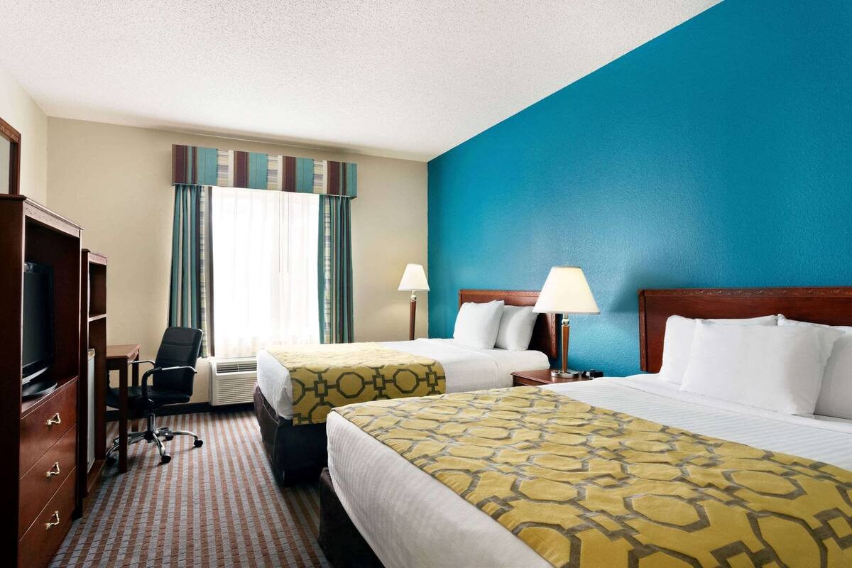 A hotel room with two beds, a desk, a chair, a TV, and a window with curtains.