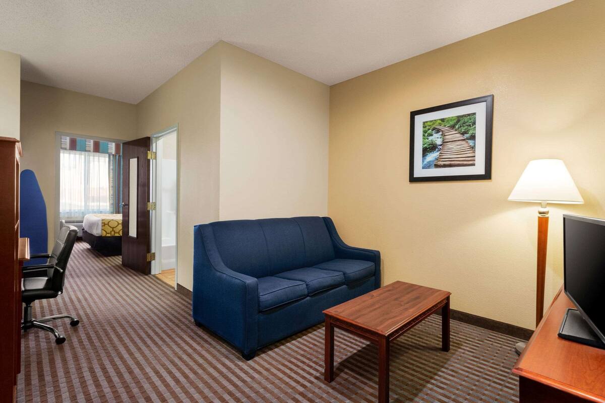 A hotel room with a blue sofa, a wooden table, a TV, and a framed picture on the wall.