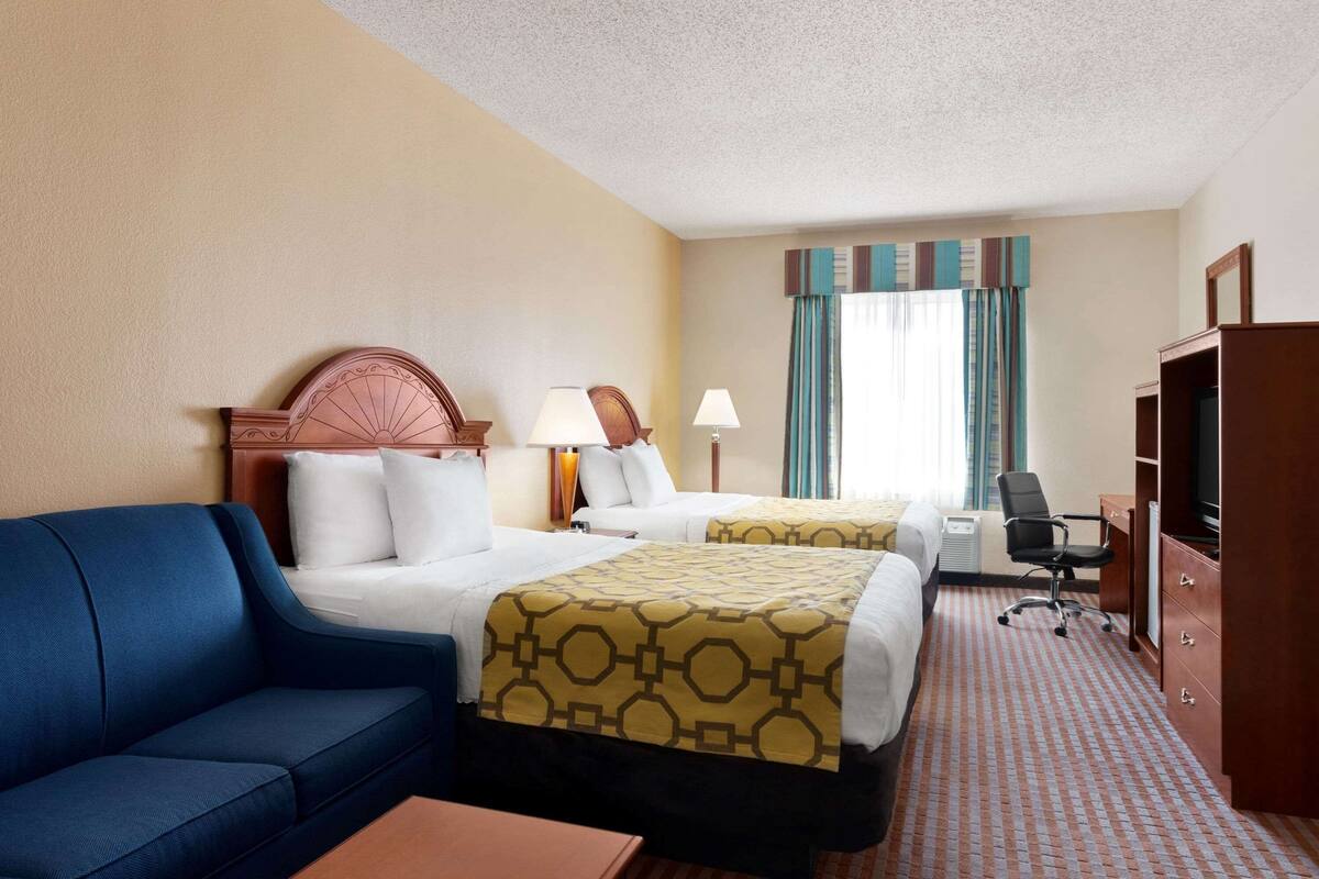 A hotel room with two beds, a blue sofa, a desk, and a wardrobe.